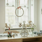 Decorative setup on a table with Christmas-themed items in a room with a window and wall art.