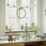 Decorative setup on a table with Christmas-themed items in a room with a window and wall art.