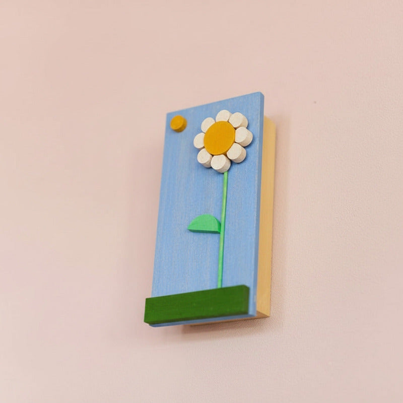 Decorative music box with a daisy motif hanging on a light pink wall 