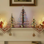 Three decorative Christmas trees with snowflake themed sections made of laser cut wooden pieces sitting on a mantlepiece