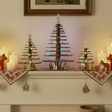 Three decorative Christmas trees with snowflake themed sections made of laser cut wooden pieces sitting on a mantlepiece